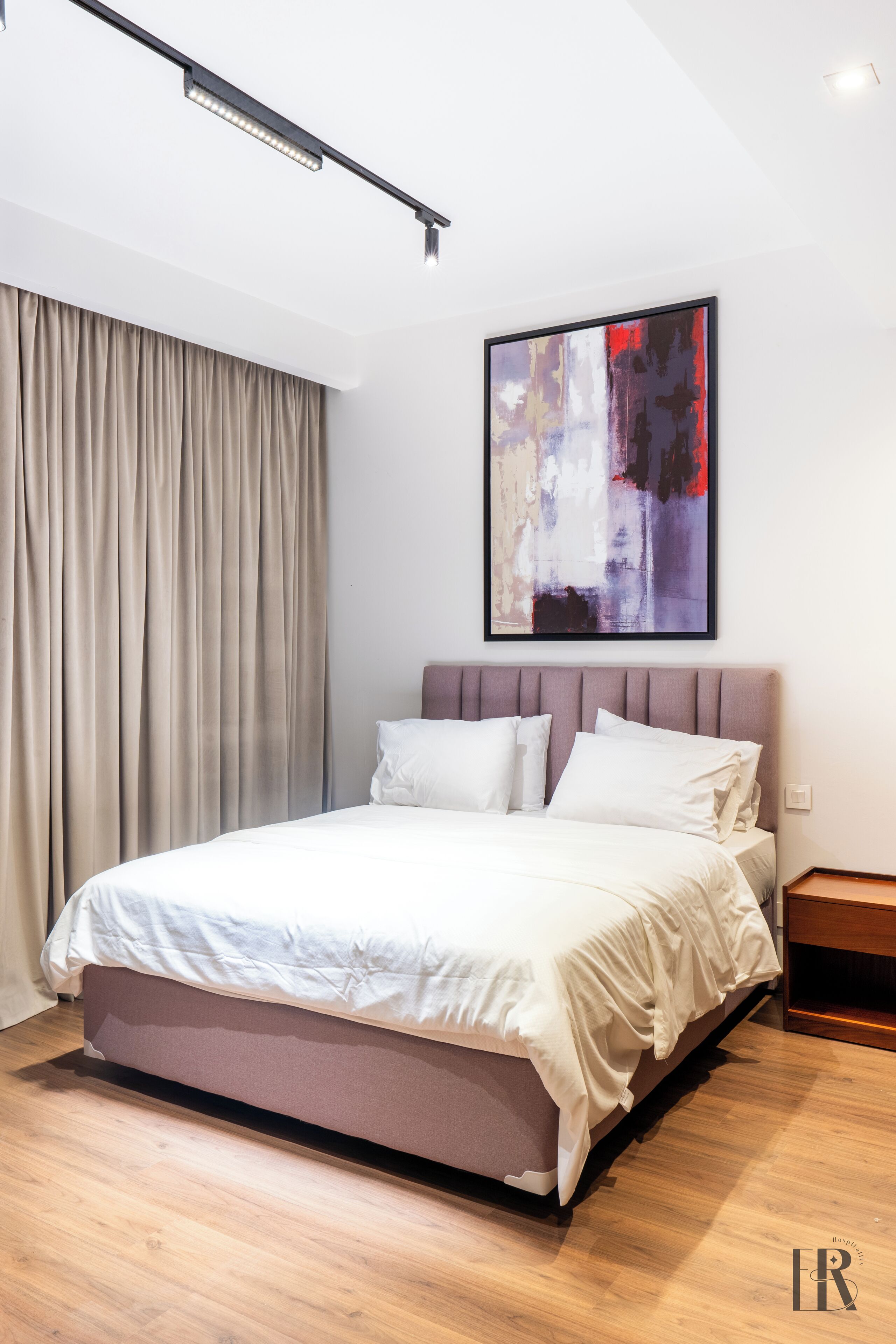 A modern bedroom with a large bed, a headboard, a painting, and a window with curtains.