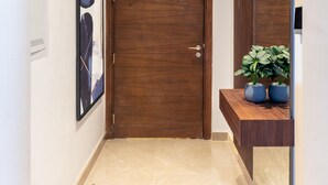 A hallway with a wooden door, a framed artwork, a mirror, and a small plant on a wooden shelf. - Easy Rental/ Serviced Apartment In CFC New Cairo (NEW Cairo Governorate)
