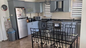 A modern kitchen with grey cabinets, a stainless steel refrigerator, a built-in oven, a microwave, and a dining area with a glass table and chairs. - 6-bedroom villa in beautiful Ölüdeniz with WiFi, AC (Ölüdeniz)