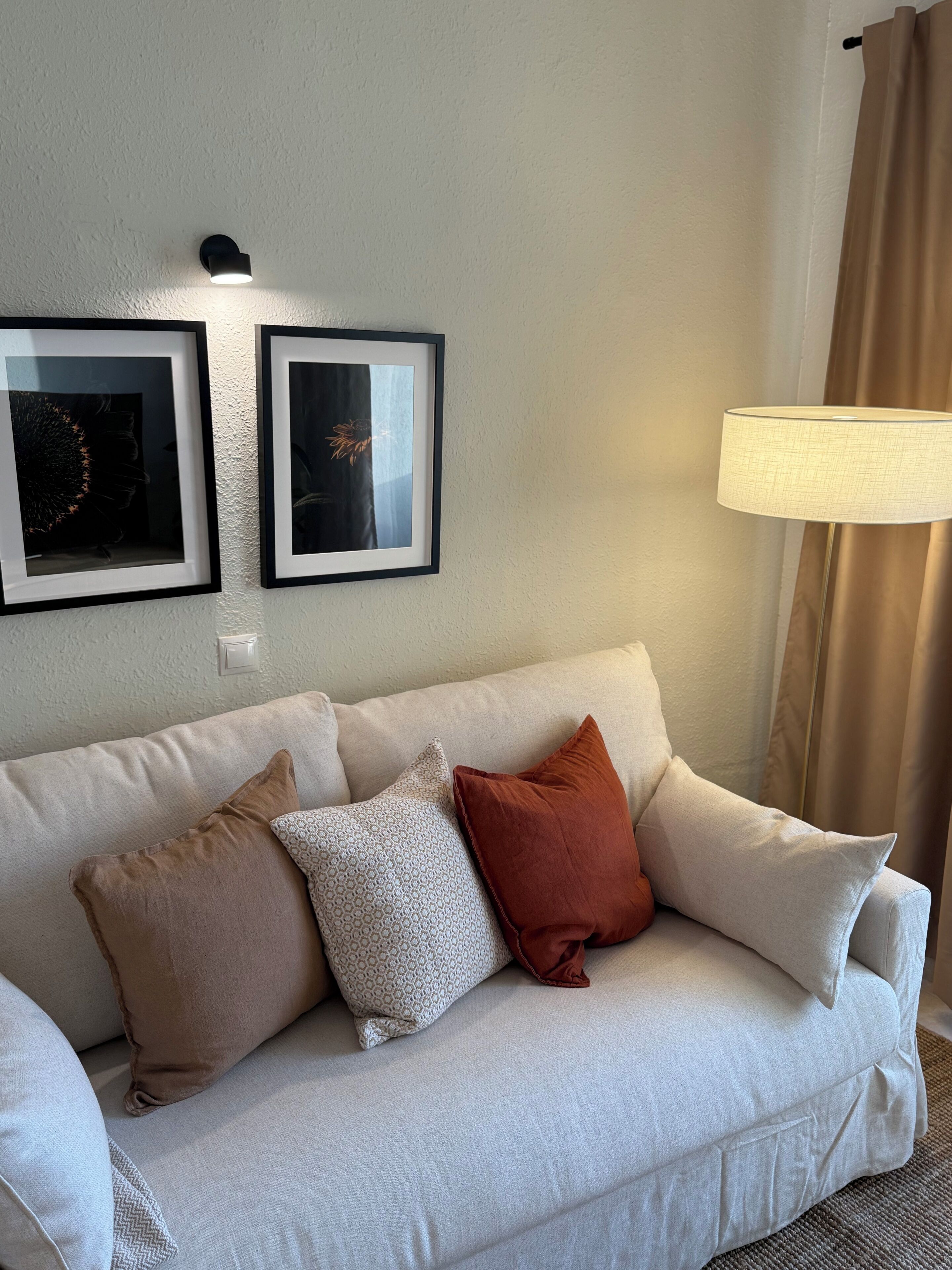 Ein weißes Sofa mit drei Kissen, einer Wandleuchte und zwei gerahmten Bildern.