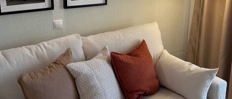 Ein weißes Sofa mit drei Kissen, einer Wandleuchte und zwei gerahmten Bildern.
