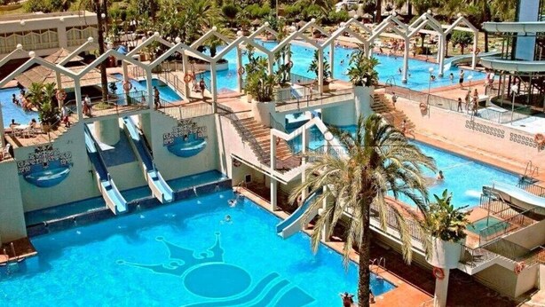 Una gran piscina exterior amb diverses tobogans i una zona de solàrium.