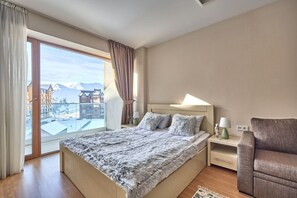 Ein Schlafzimmer mit einem großen Bett, einem Nachttisch, einer Lampe und Blick auf Gebäude und Berge durch eine Schiebetür.