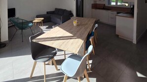 A modern kitchen with a central island, a dining area with a wooden table and chairs, and a living area with a sofa and chairs.