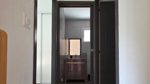A narrow hallway leading to a bathroom with a wooden floor and a dark door.