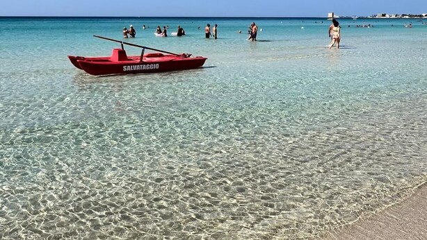 A clear beach with a red boat labeled "SALVATAGGIO" anchored near the shore.