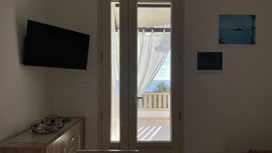 A room with a bed, a TV mounted on the wall, a door leading to a balcony, and a small table with a basket.