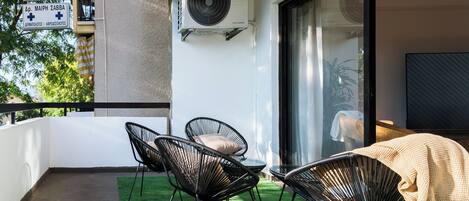 A balcony with a green artificial turf, two black chairs, a table, and a large air conditioning unit.