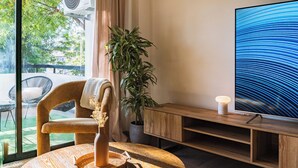A modern living room with a large flat-screen TV, a potted plant, a wicker chair, and a wooden entertainment unit. - City Center Modern Boho Stay (Nicosia)