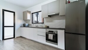 A modern kitchen with white cabinets, a stainless steel refrigerator, a built-in oven, and a window above the sink. - City Center Modern Boho Stay (Nicosia)