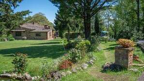 A stone house with a tiled roof, surrounded by a well-maintained garden with various plants and a small pond.