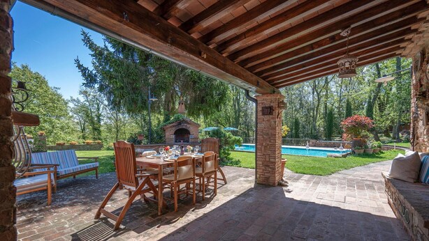 An outdoor patio with a brick table and chairs, a brick fireplace, and a pool in the background.