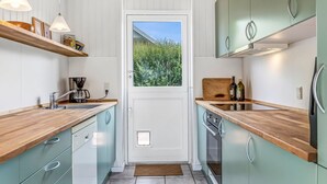 A compact kitchen with wooden countertops, light green cabinets, and a window with a view of greenery.
