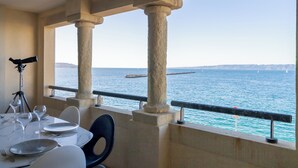 A dining area with a table set for two, overlooking a body of water with a distant landmass and a pier. - Luxury and sea view, 3 bedrooms, plage des Catalans (Marseille)