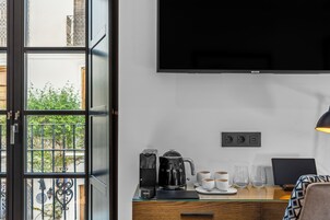 A hotel room with a large window, a coffee maker, a kettle, a TV, and a desk with a laptop and glasses.