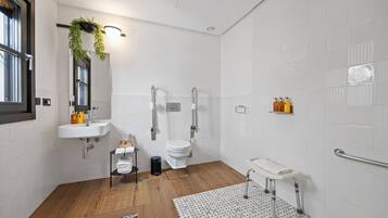 Un bany modern amb terra de fusta, un lavabo blanc, un vàter i una zona de dutxa.
