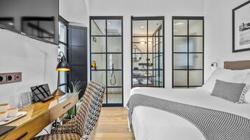 Een moderne hotelkamer met een groot bed, een bureau met een lamp en een uitzicht door glazen deuren naar een badkamer.