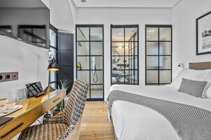 Een moderne hotelkamer met een groot bed, een bureau met een lamp en een uitzicht door glazen deuren naar een badkamer.