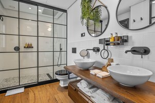 Een moderne badkamer met een douchecabine van glas, twee grote witte wastafels en een houten wastafelmeubel.