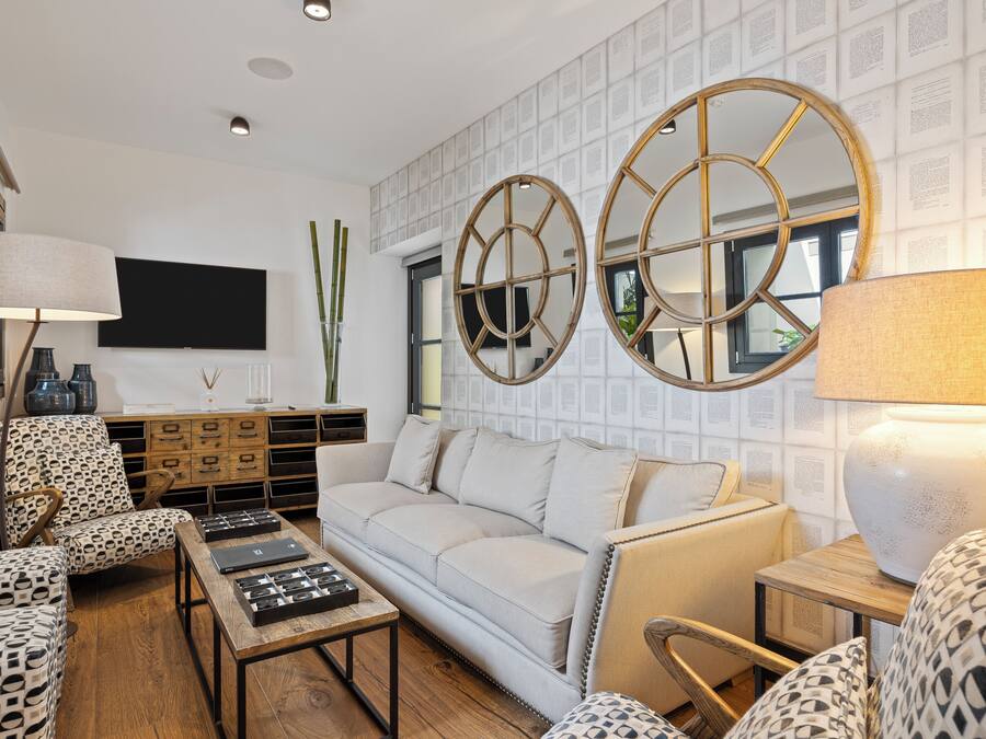 Een moderne woonkamer met een bank, gestreepte stoelen, een bijzettafeltje en decoratieve spiegels.