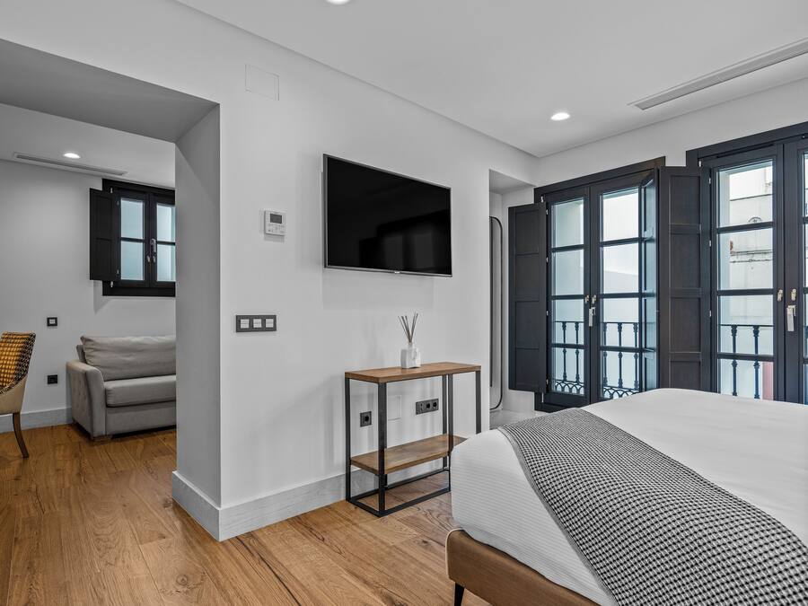 A modern bedroom with a large bed, a TV mounted on the wall, and a window with a view of the outside.