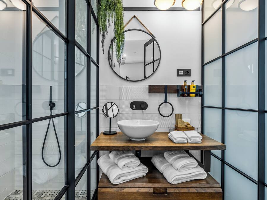 A modern bathroom with a glass shower enclosure, a wooden vanity with a white bowl sink, and a mirror above it.