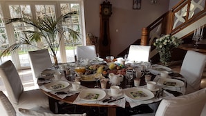 A dining table set for a meal with white chairs, surrounded by a window with a view of greenery. - Ruthellen's Home (Planegg)