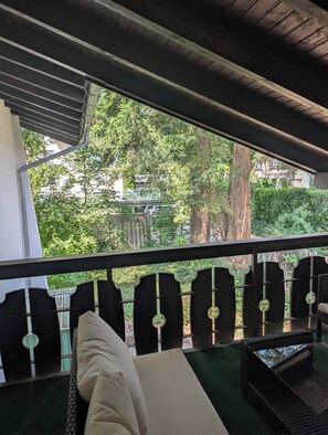 A balcony with a view of trees and a building. There are chairs and a table on the balcony. - Ruthellen's Home (Planegg)