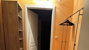 A hallway with a wooden floor, a grey rug, a wardrobe, and a clothing rack. - Ruthellen's Home (Planegg)