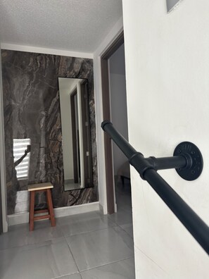 Un couloir avec un mur en marbre, un tabouret en bois et une main courante noire.