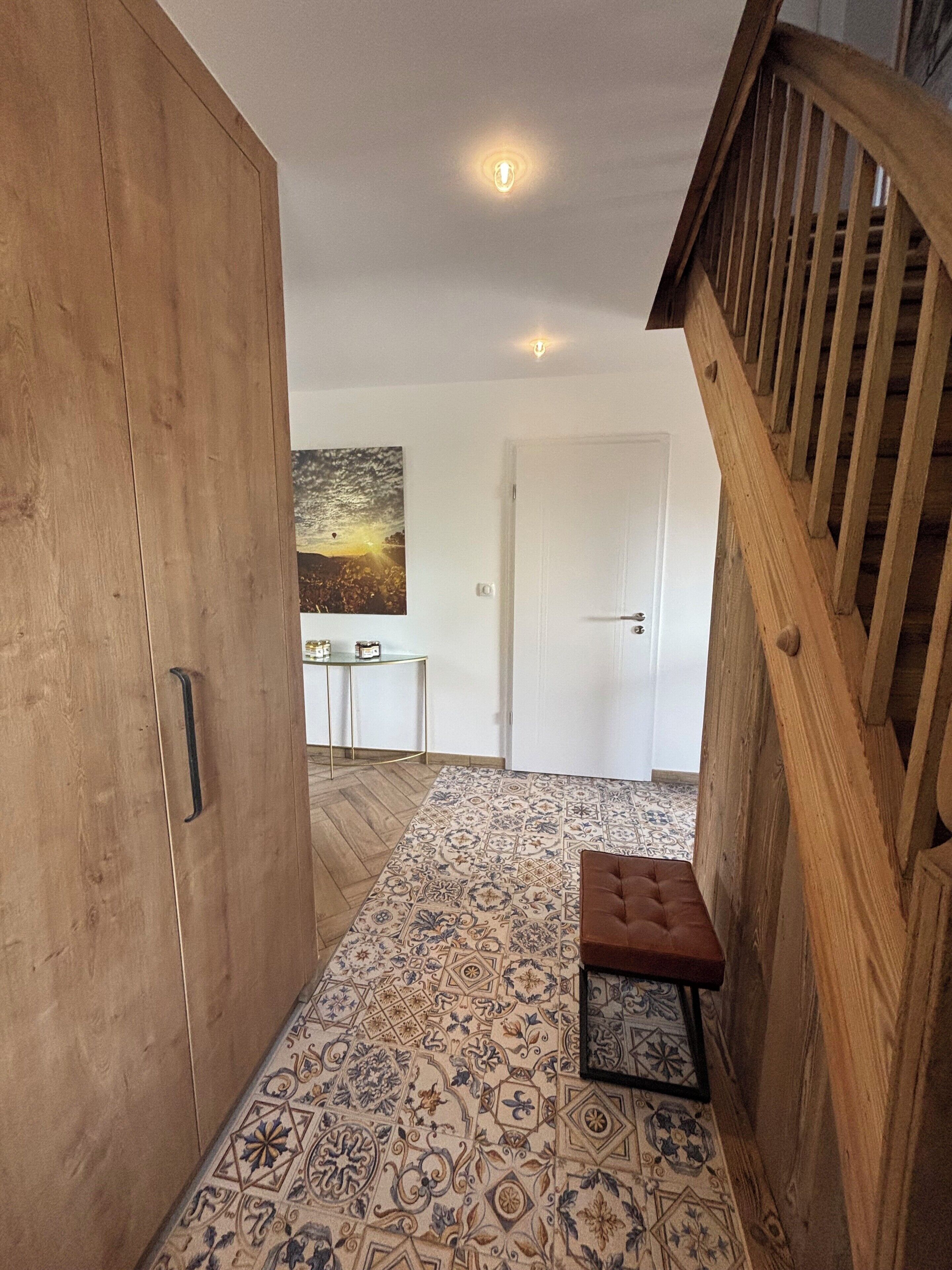 Un corridoio con pavimento decorato, un armadio in legno, una panca e un quadro appeso al muro.