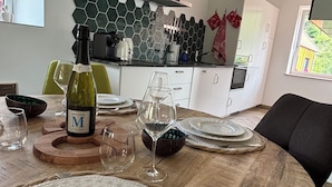 Een eettafel gedekt met borden, glazen en een fles wijn, met een moderne keuken op de achtergrond.