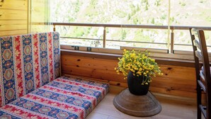 Un interior de madera con un sofá estampado, una planta en maceta y vistas de un paisaje montañoso.