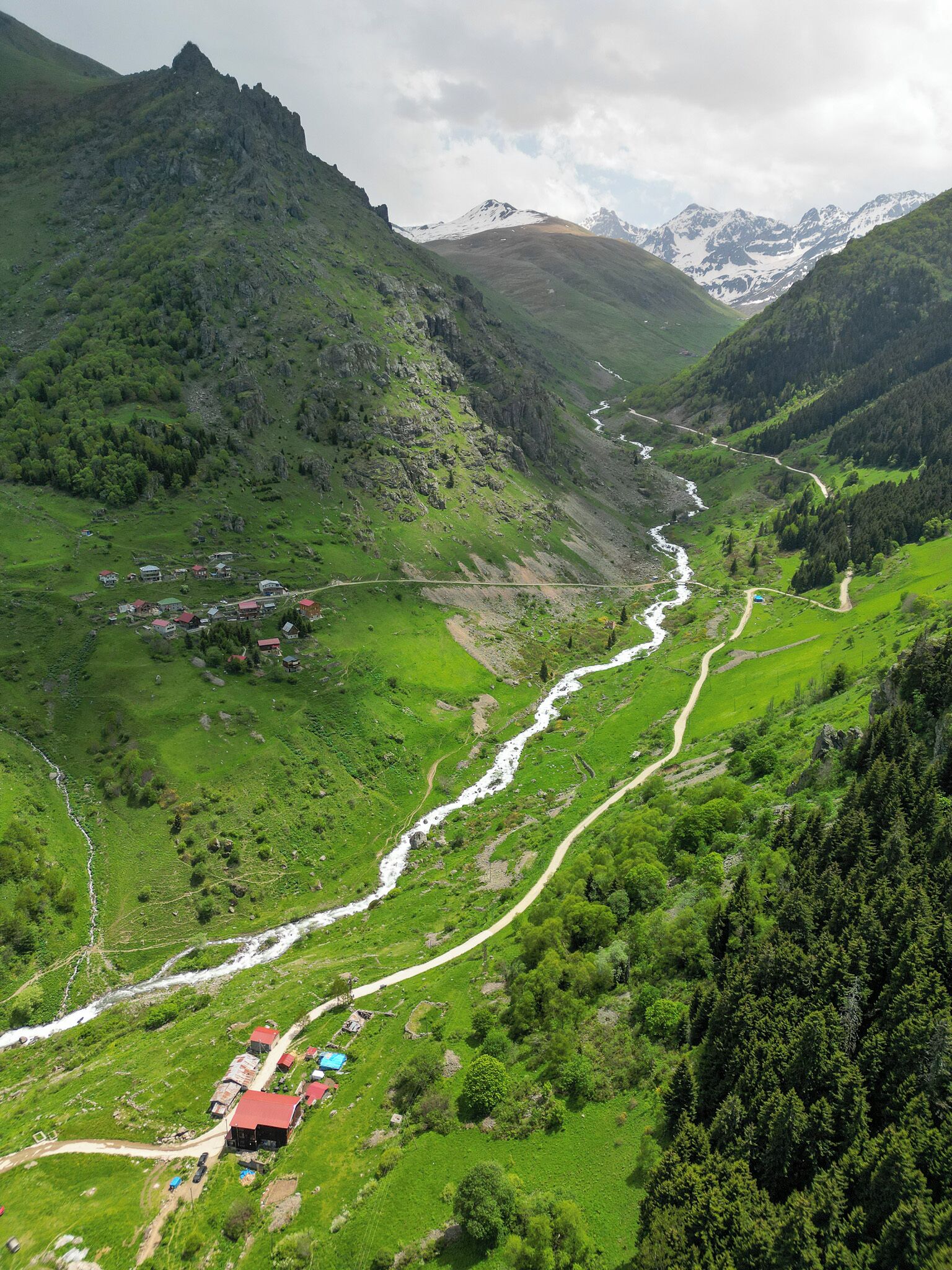 A mountainous landscape with a river, green valleys, and scattered buildings.