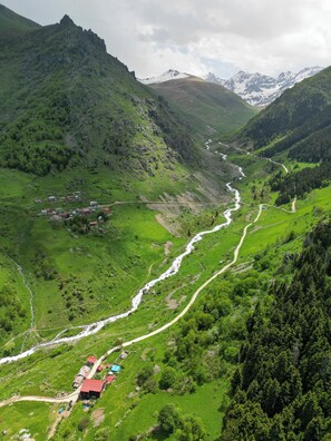A mountainous landscape with a river, green valleys, and scattered buildings. -  Palam Pansiyon (Camlihemsin)