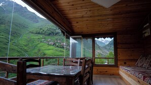 Una cabaña de madera con comedor y sofá, con vistas a un valle verde y montañas.