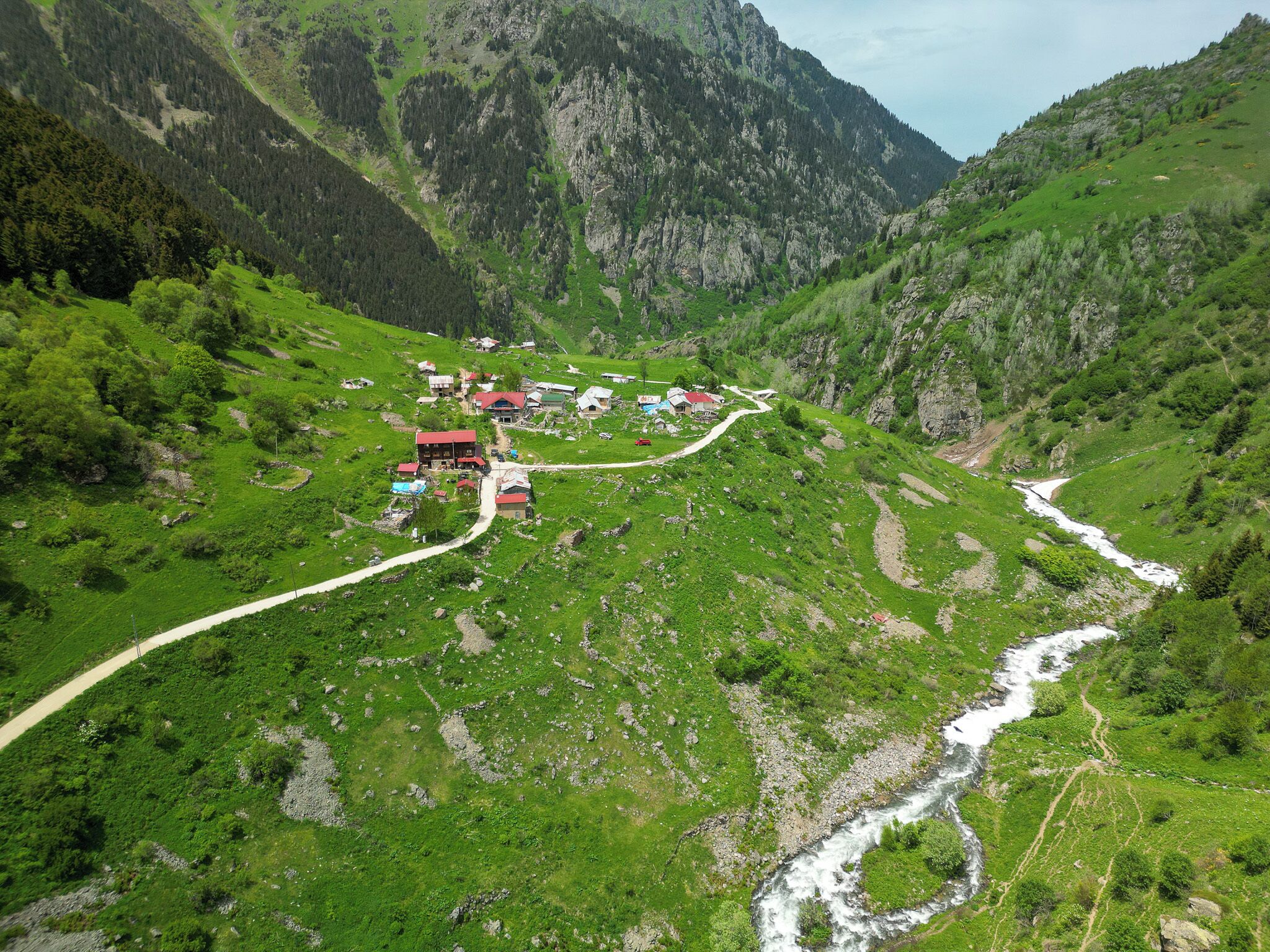 A mountainous landscape with a small settlement featuring several buildings, a winding road, and a river.