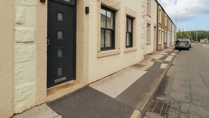 Un hilera de casas urbanas con puerta negra, ventanas con contraventanas y cielo despejado.