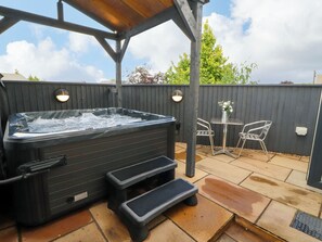 A hot tub under a wooden pergola with two steps leading up to it, a table with chairs, and a wooden fence in the background. - Lakes View Apartment 1 (Carnforth)