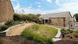 A stone building with a grassy courtyard, a wooden table, and chairs.