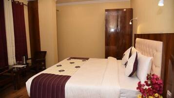 A hotel room with a large bed, a wooden headboard, a desk with a chair, and a window with curtains.