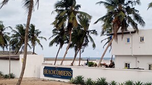 «Beachcombers»-niminen kyltti, josta avautuu näkymä rannalle ja palmuille.