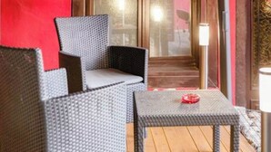 Een set rieten stoel en tafel op een houten terras, met een rode muur op de achtergrond.