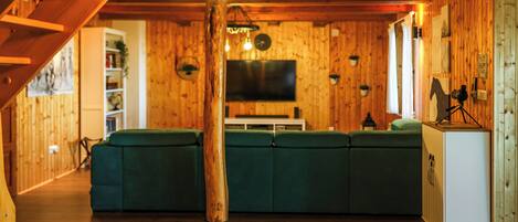 A wooden interior with a green sofa, wooden beams, a television, and a wooden cabinet.