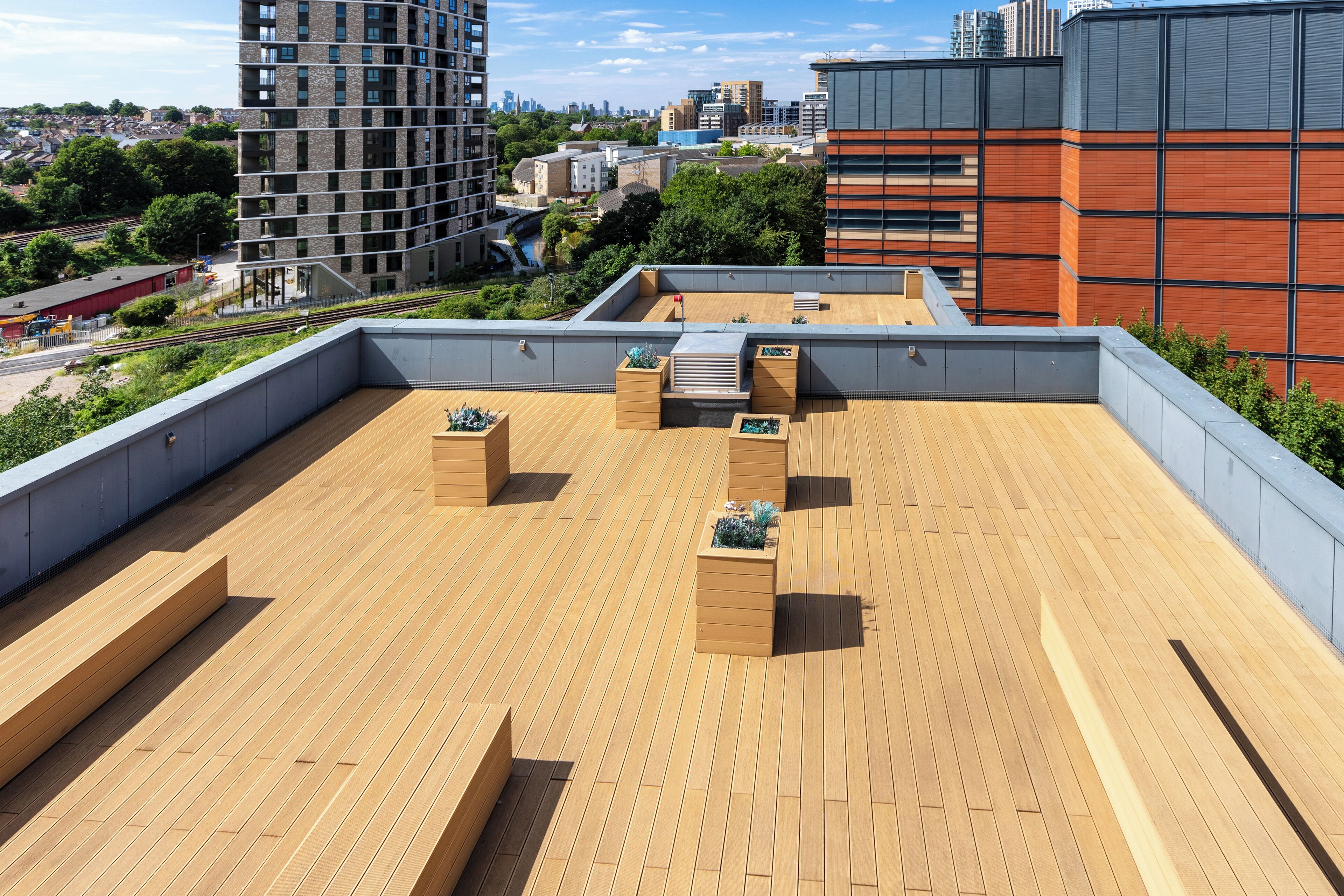 A rooftop terrace with wooden flooring, planters, and a view of the cityscape.