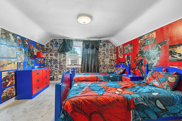 A bedroom with two beds, a dresser, and walls covered in comic book art.