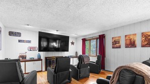 A living room with a flat-screen TV, black leather sofas, wooden flooring, and movie-themed wall decorations. - Your friendly neighborhood Airbnb (Rockford)