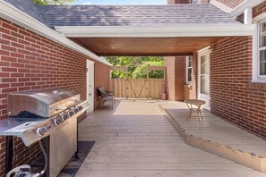 A backyard with a barbecue grill, a covered patio, and a wooden fence.