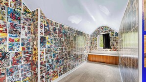 A room with a wall covered in comic book panels, a window, and a bed with a wooden headboard. - Your friendly neighborhood Airbnb (Rockford)
