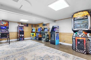 A room with arcade games, a large rug, wooden paneling, and a ceiling light.
